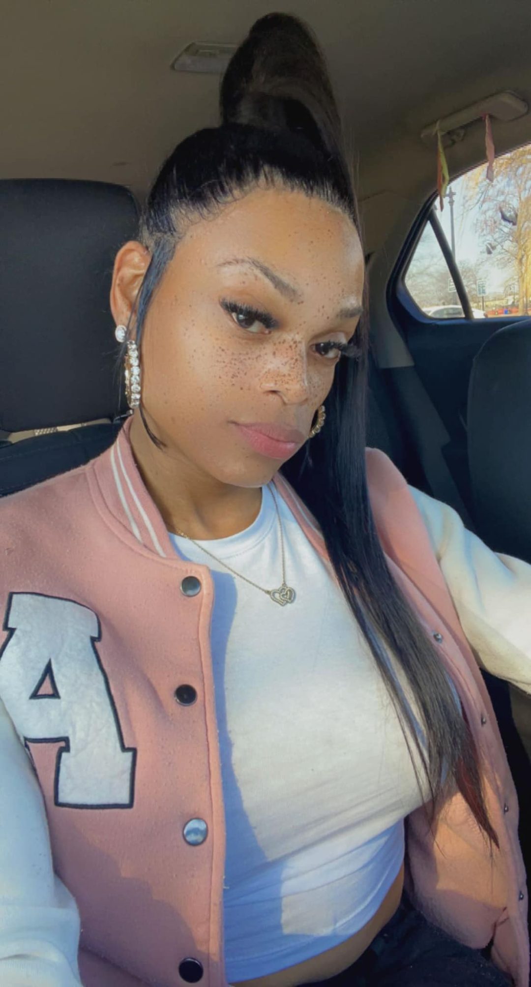 Black trans woman Ashia Davis wearing a white top, a pink sports jacket and a silver heart chain.
