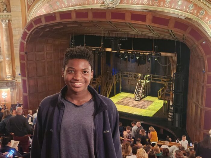 a black teen male standing in a theater with the stage in the background